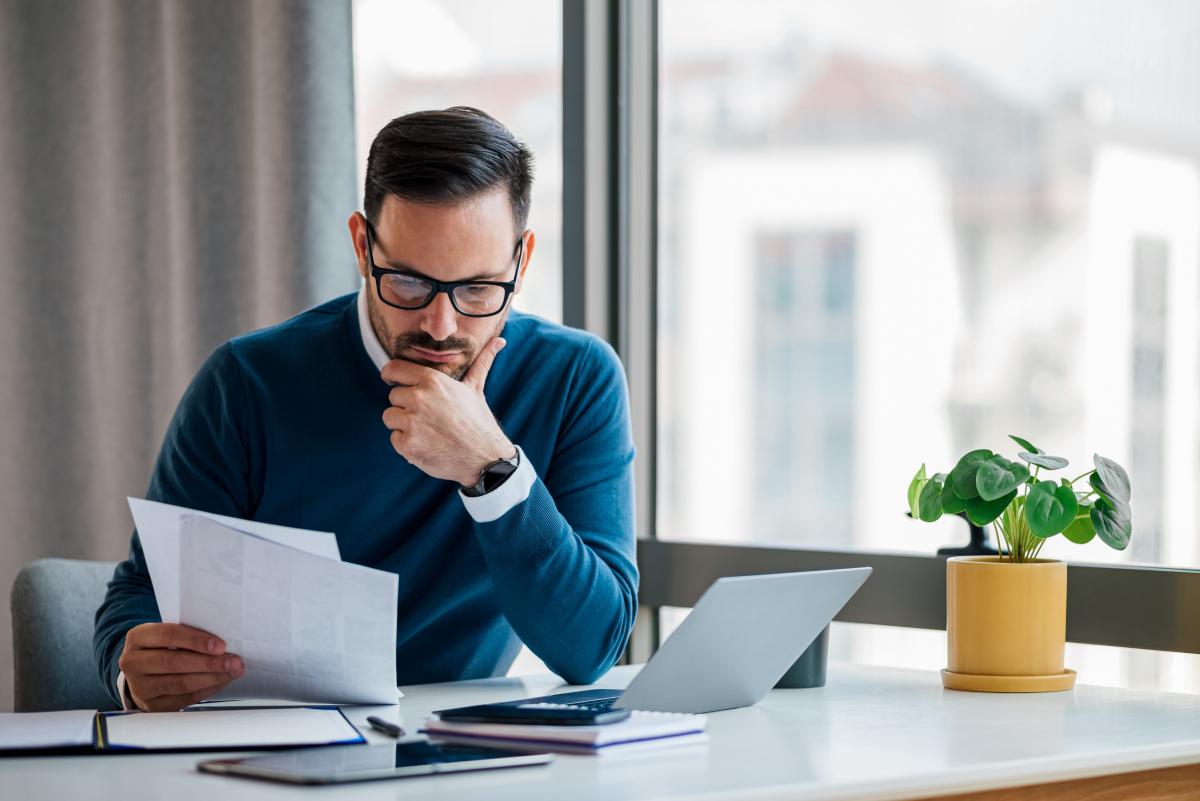 Man sitting at his desk with his laptop open, and looking at some papers