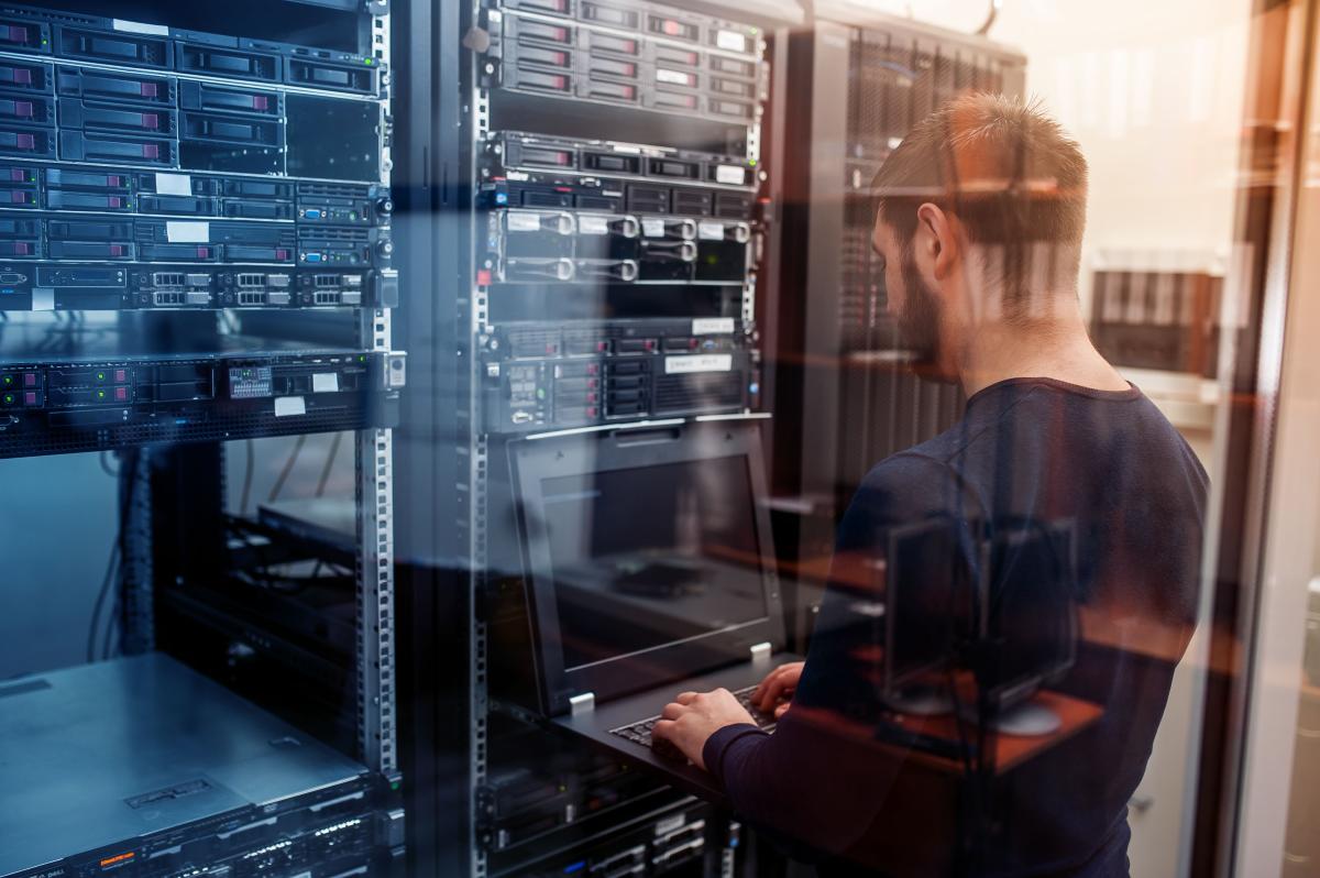 Network administrator typing on laptop inside a server closet