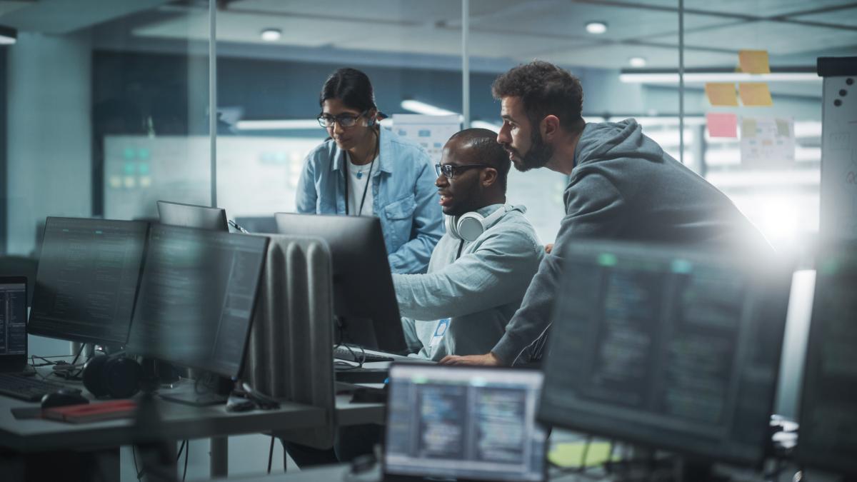 A woman and two men all looking at a computer screen inside an office