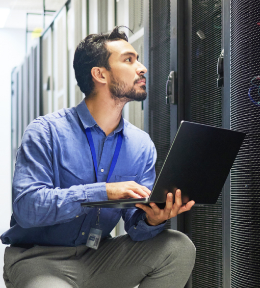 A security engineer working on a laptop near large servers